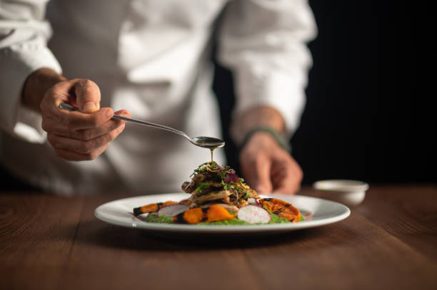 Professional private chef pouring gourmet sauce on a plated meal in a luxury home kitchen.