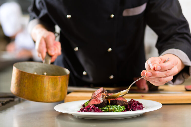 A professional private chef carefully pouring sauce over a perfectly seared steak, demonstrating the precision and culinary excellence expected in a private household placement.